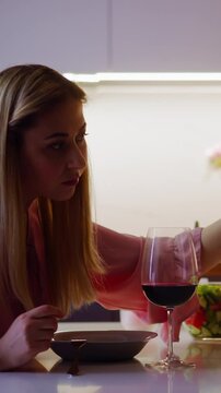 Suspicious blonde woman adds poisonous powder into guest red wine looking back at served romantic date in kitchen at home slow motion