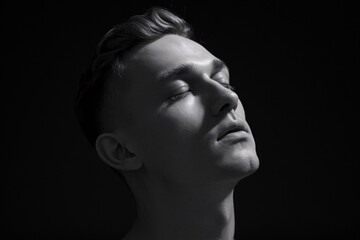 Serene Monochrome Portrait: A young man with eyes closed, bathed in dramatic chiaroscuro lighting, evokes a sense of peace and contemplation. 