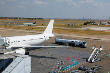 airplane parked while fuel tanker arrives on bustling runway