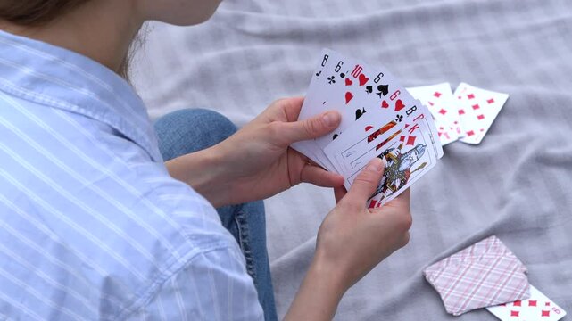 A young woman playing cards chooses how to move, looks at the trump card, and puts the card on the deck outdoors. Concept of board card games, getting fun, entertainment