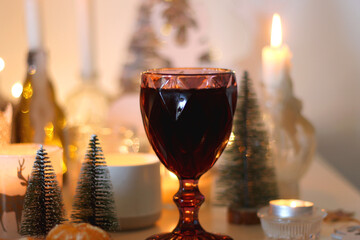 Various Christmas decorations, cookies, chocolate, nuts and tangerines, wine glasses and lit candles on the table. Holiday hygge at home. Selective focus.