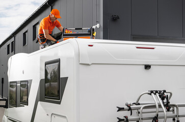 Man Working on the Roof of a Camper Trailer at a Repair Facility During Daylight Hours