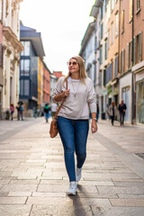 Beautiful middle-aged long-haired woman wearing jeans, beige sweater, sunglasses and leather...