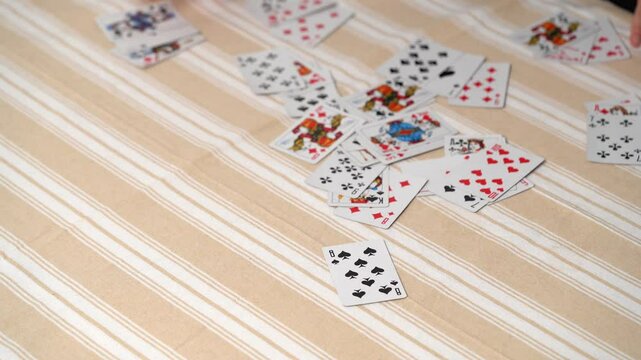 The hands of a young woman collect cards from a table with a tablecloth, shuffling them for the next game. Entertainment concept, having fun, card games