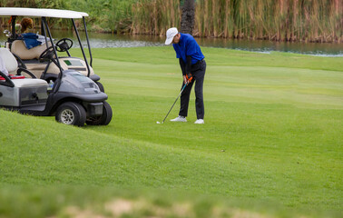 a white golf ball on a tee and a green field ready to be hit with a wood golf stick as a start to a game of golf.