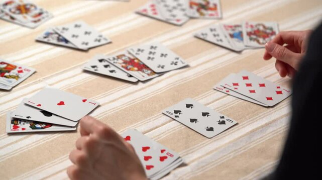 Hands of a young woman choosing and stacking cards while playing solitaire at the table. Entertainment concept, having fun, card board games, poker