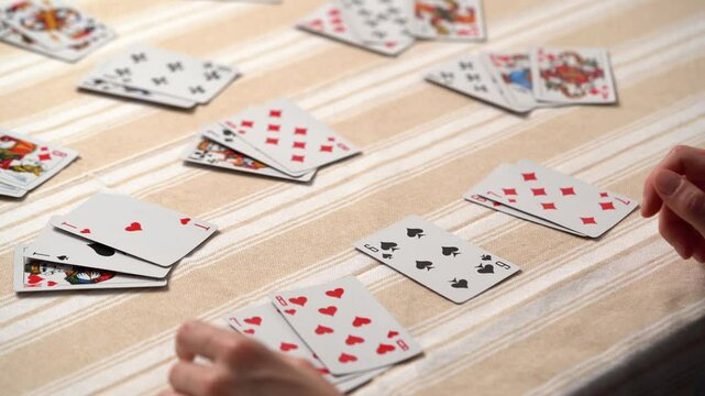 Hands of a young woman choosing and stacking cards while playing solitaire at the table. Entertainment concept, having fun, card board games, poker