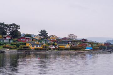 Fototapeta premium Oslo, Norway - October 20, 2024: Oslofjord (Oslofjorden), view of summer houses and cottages. Frame houses for recreation. Hut among the forest and rocks. Multicolored private houses.