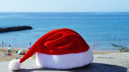 Santa Claus hat in front of the sea with blue sky while tourists on the beach enjoy the warm sun of the tropical climate in December in the Canary Islands