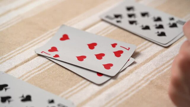 Close-up of a young woman's hand picking and stacking cards while playing solitaire at the table. Entertainment concept, having fun, card board games, poker
