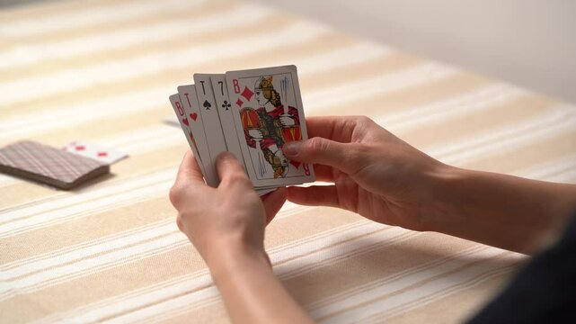 Close-up of a young woman's hand holding cards and choosing how to move, looking at the trump card, and placing the card on the deck at table. Concept of board card games, getting fun, entertainment