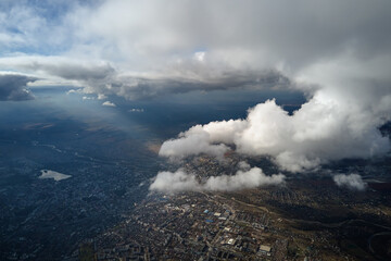 Aerial view from airplane window at high altitude of distant city covered with puffy cumulus clouds...