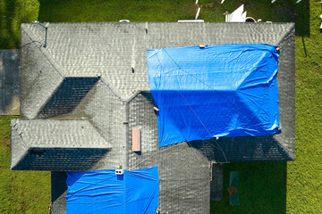 Aerial view of damaged in hurricane Ian house roof covered with blue protective tarp against rain...