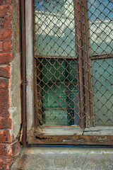 Rusted metal grid guards a weathered glass window in an old structure