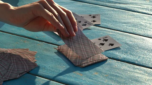 Hands of a young woman take a card from a deck while playing a card game at a blue table outdoors. Concept of entertainment, having fun
