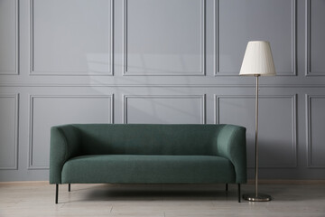 Comfortable sofa and lamp near grey wall in room