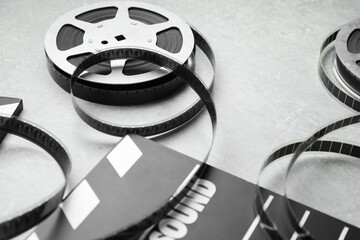 Movie clapper and film reels on grey textured table, closeup