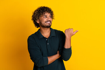 Confident young man points aside with a smile on his face against a vibrant yellow background