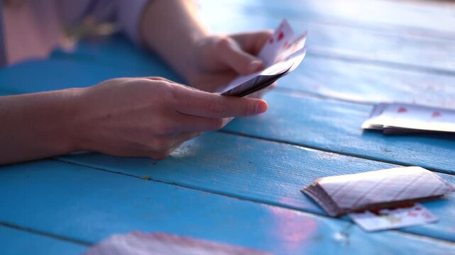 Hands of a young woman take a card from a deck while playing a card game at a blue table outdoors. Concept of entertainment, having fun