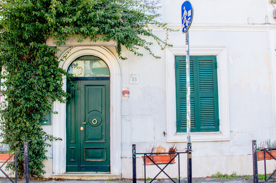 Charming entrance with green door and window  framed by light grey wall and greenery in the Pigneto neighborhood of Rome. Italy, 2023.