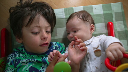 Young boy and baby lying on the floor, gazing at each other, baby smiling with joy, highlighting a...