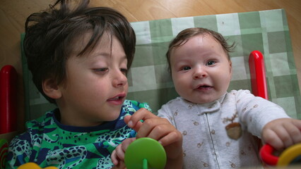 Young boy and baby lying on the floor, gazing at each other, baby smiling with joy, highlighting a...
