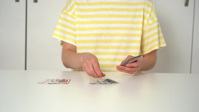 A young woman in a yellow t-shirt dealing classic cards from a deck for playing solitaire at a table. The concept of board card games, having fun, entertainment, poker.