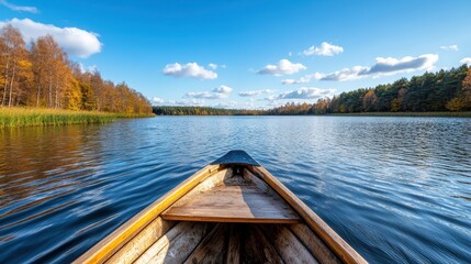Obraz premium The front view from a wooden boat looking across a calm lake, surrounded by vibrant autumn trees, showcasing a tranquil and serene natural setting.