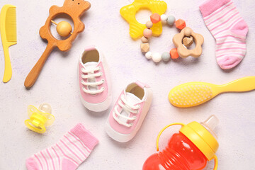 Stylish baby shoes with socks, rattles, brushes, bottle of milk and pacifier on grunge white background