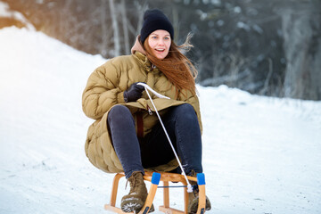 Portrait young adult happy woman enjoy having fun riding vintage wooden retro sledge mountain hill cold winter sunny day. Female joyful person sledding downhill outside at Christmas season