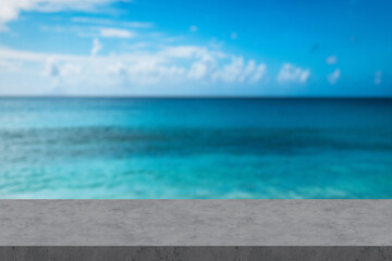 Fototapeta premium Empty white marble table with blur blue sky and sea bokeh background with green leaf foreground, Mock up template for display or montage of product or content use as banner in social media ads