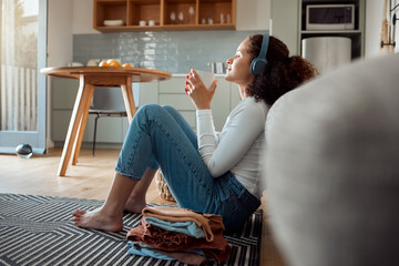 Woman, headphones and home with music, chores break and morning on floor with rest in living room. Audio, coffee and hot drink with listening, podcast and home cleaning on relax weekend in break