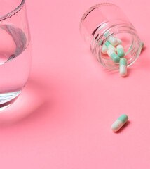 Medicines, pills and a glass of water next to it, on a light background and inside a small glass container.