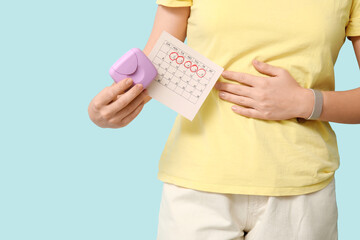 Young woman with tampon box and calendar on blue background, closeup