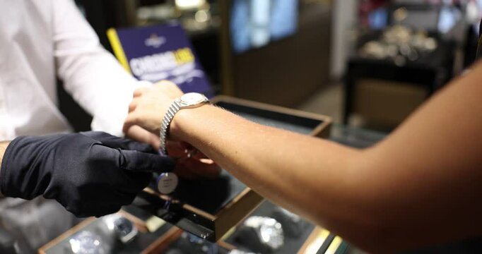 Watch seller in black gloves adjusts wristwatch on woman wrist in jewelry store. Salesperson provides quality services to lady customer