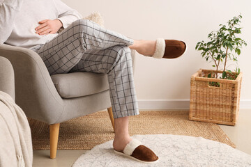 Fototapeta premium Man in slippers and pajamas sitting on soft armchair in living room