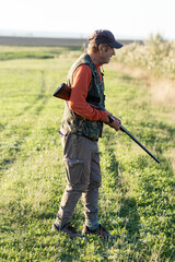 Mature hunter man holding a shotgun and walking through a field