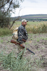 Mature hunter man holding a shotgun and walking through a field