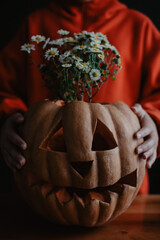 Teenager girl holding carved Halloween pumpkin with flowers inside, close up