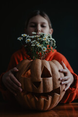 Teenager girl holding carved Halloween pumpkin with flowers inside, close up