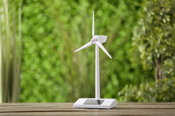 Wind turbine model on wooden table against green nature background