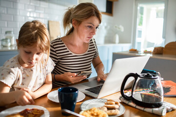 Mother working on laptop while family has breakfast in kitchen