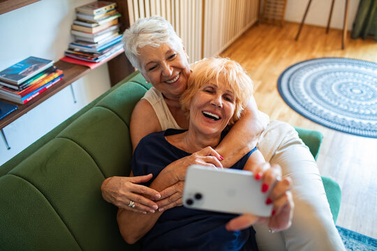Senior lesbian couple taking a selfie together on a couch