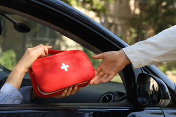 Woman on passenger seat passing first aid kit to person outside car