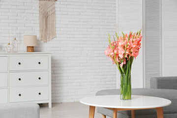 Vase with gladiolus flowers on table in light living room