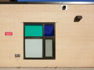 A beige brick wall with black metal frame window, ventilation pipe, light fixture and fire...