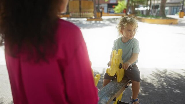 Woman watching son play on a seesaw at an urban playground, capturing a joyful family moment in the city exterior environment.