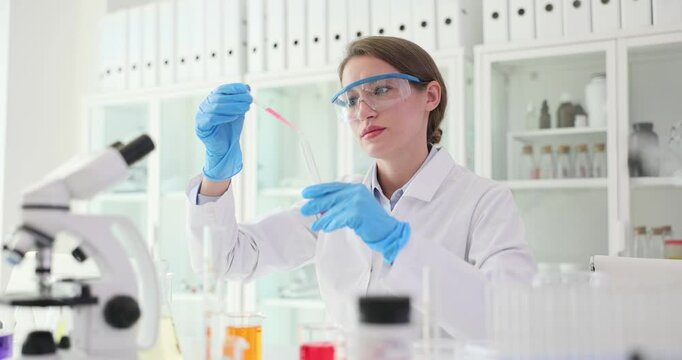 Woman scientist carefully drops reagent into glass tube with pipette at workplace slow motion. Technician in gloves prepares specimen for research