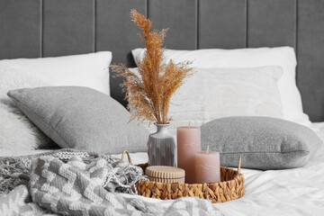 Wicker tray with candles and pampas grass on bed