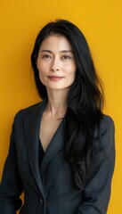 Obraz premium Confident Woman with Long Black Hair in Grey Blazer Against Vibrant Yellow Backdrop